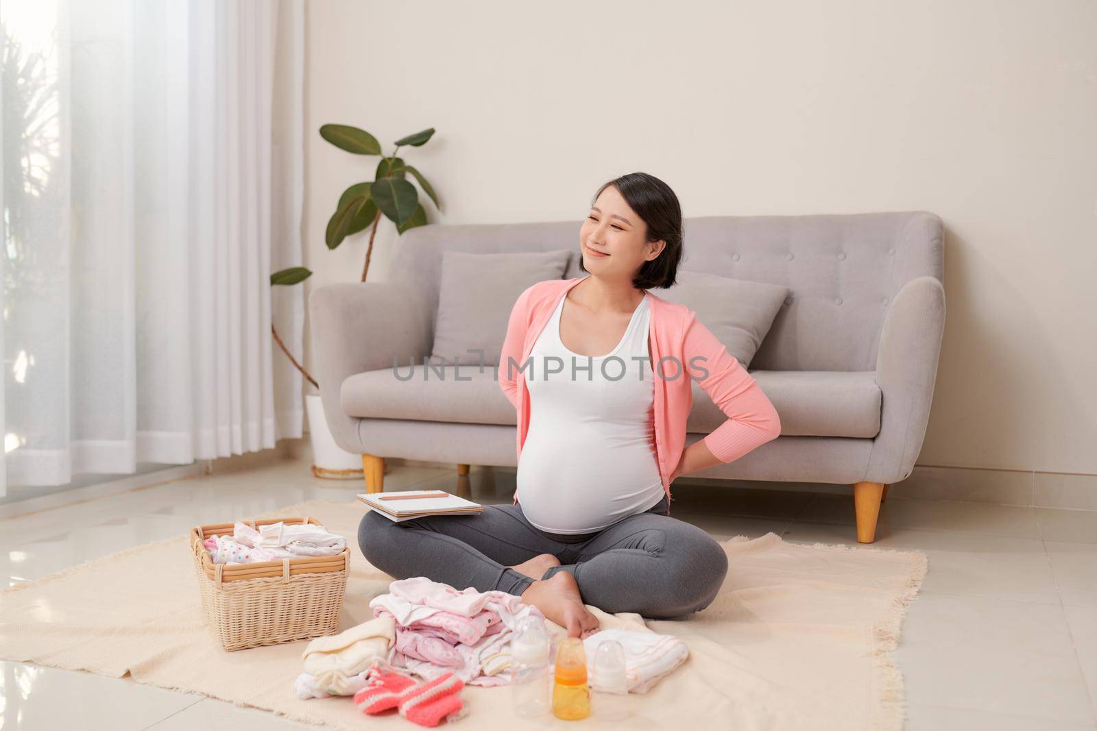 Happy young mother with travel luggage of baby clothes at home by makidotvn