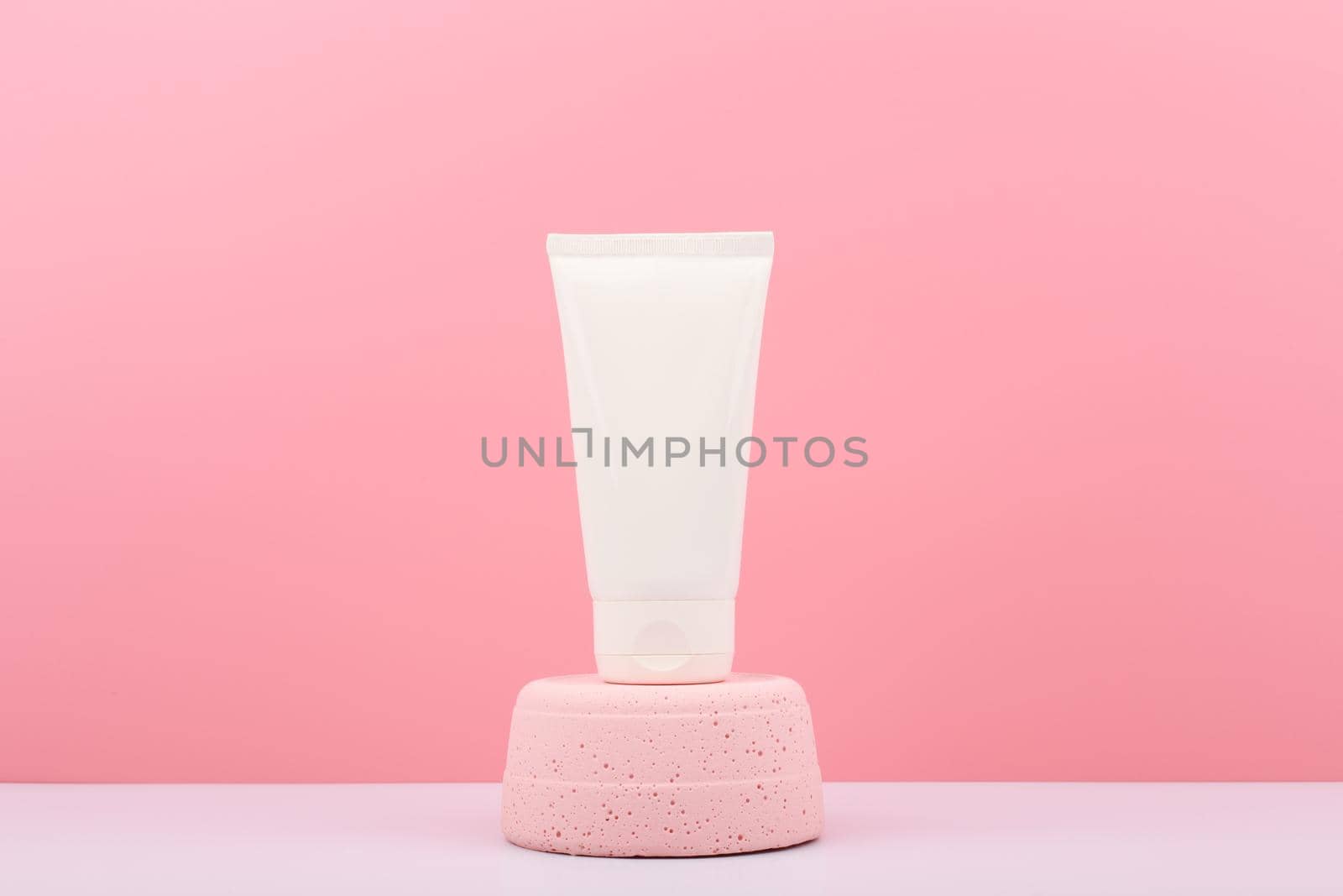 White plastic cosmetic tube with cream, balm, mask, scrub or lotion on pink pedestal against pink background with copy space. Concept of natural organic skin care products 
