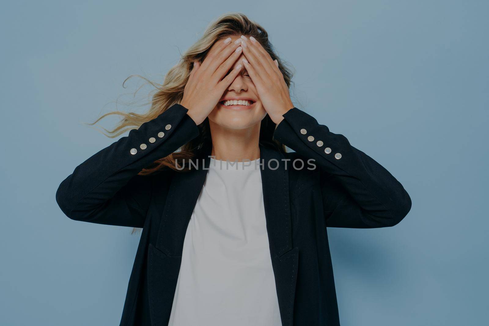 Funny blond beautiful female closing eyes with her hands, having fun and playing hide and seek by vkstock