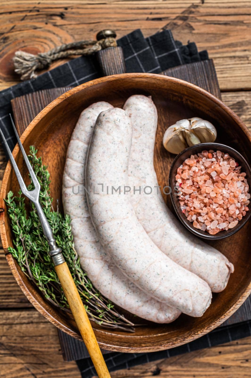 Raw Munich traditional white sausages in a wooden plate with herbs. wooden background. Top view by Composter