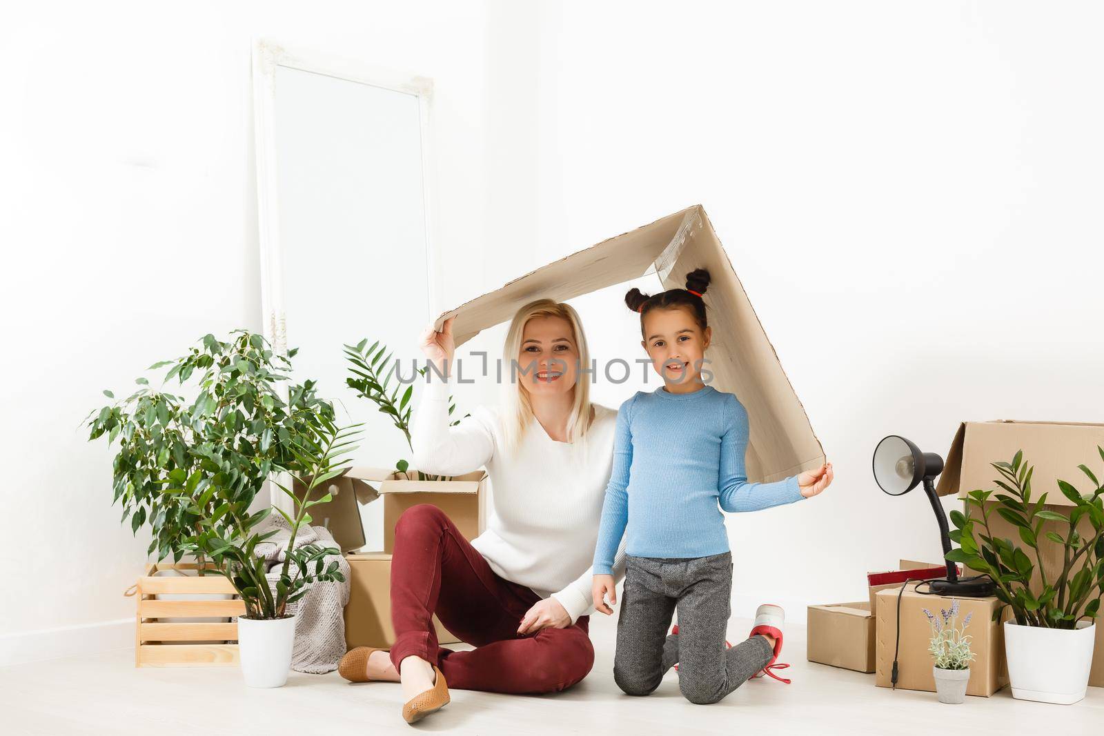 Happy mother and daughter sitting under cardboard roof at home. Insurance concept by Andelov13