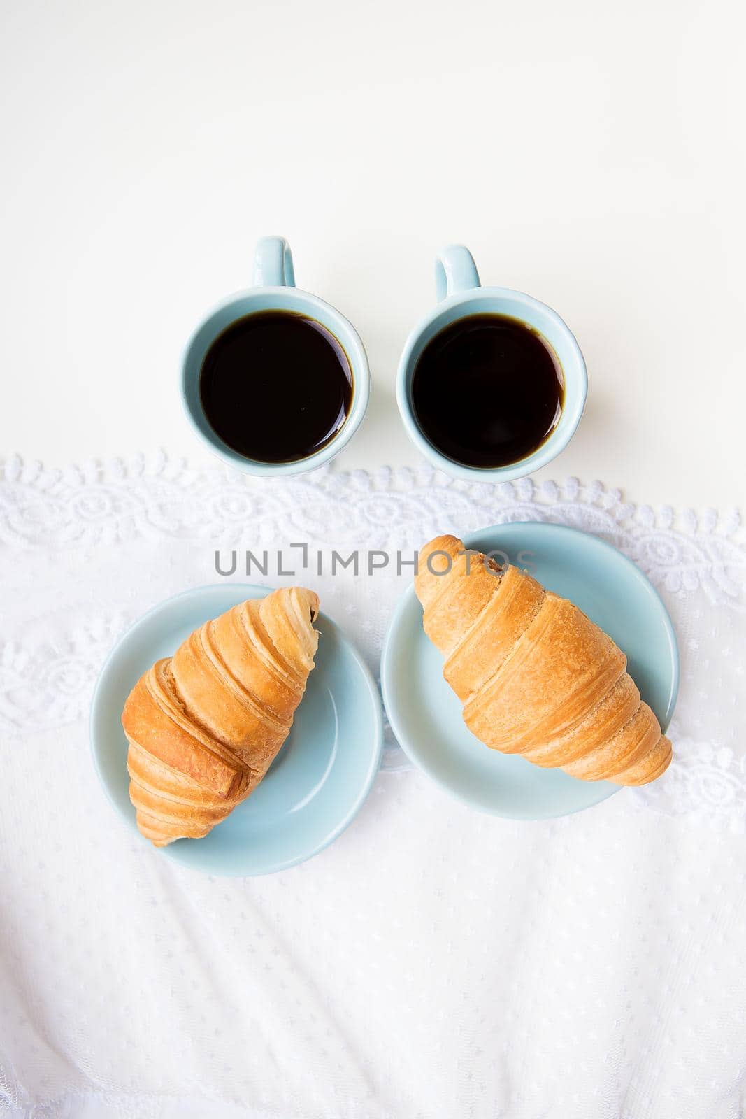 two cups of coffee with croissants on the background of laces on a white background, close-up