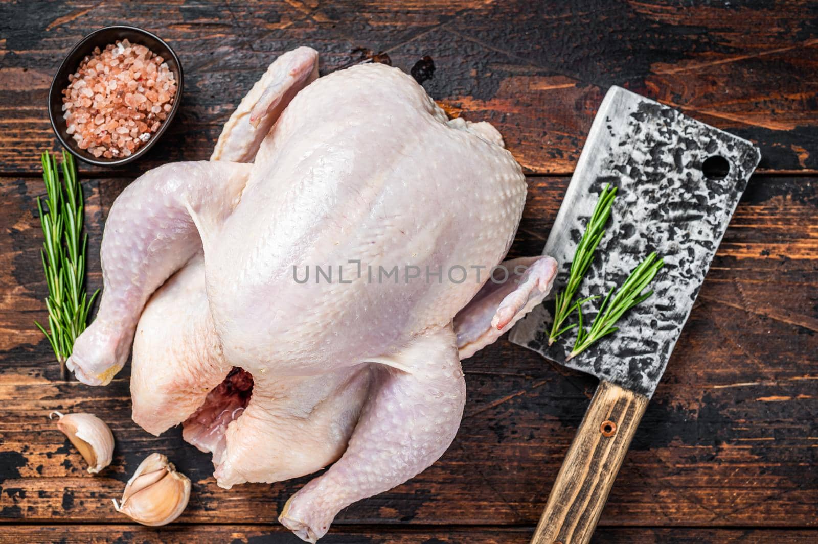 Whole chicken, raw poultry on a butchery table with meat cleaver. Dark Wooden background. Top view.