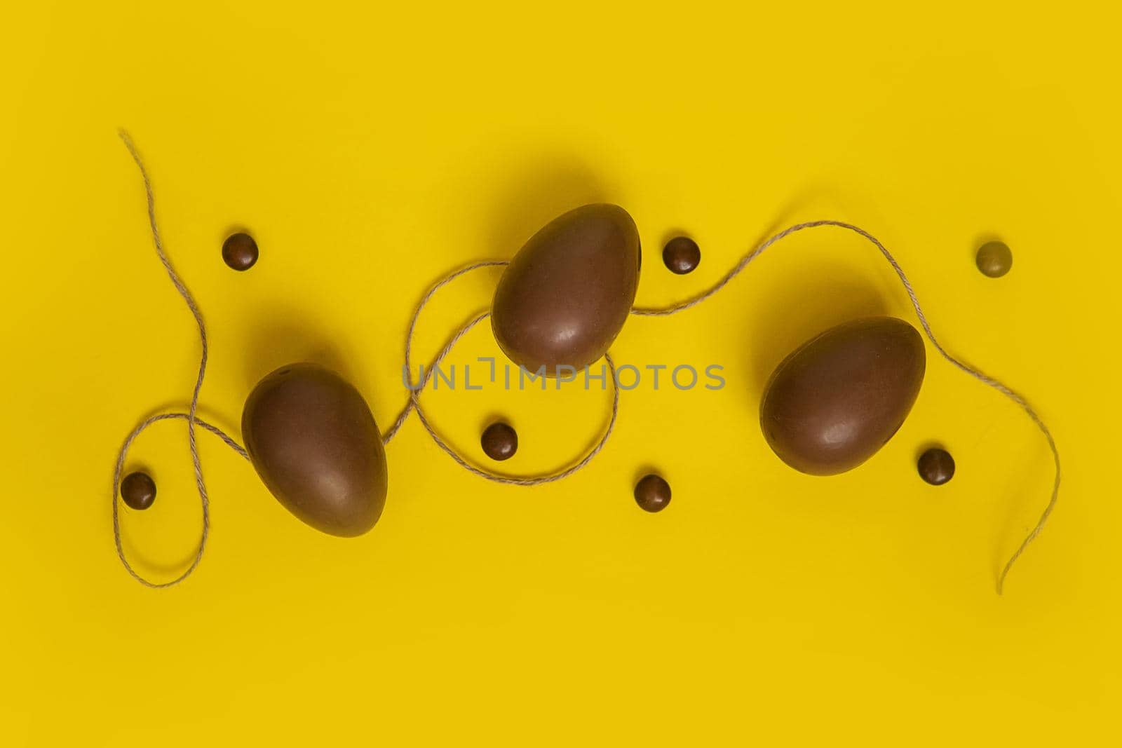 Flat lay composition with chocolate Easter eggs and chocolate sweets on yellow background. View from above, empty space for text.