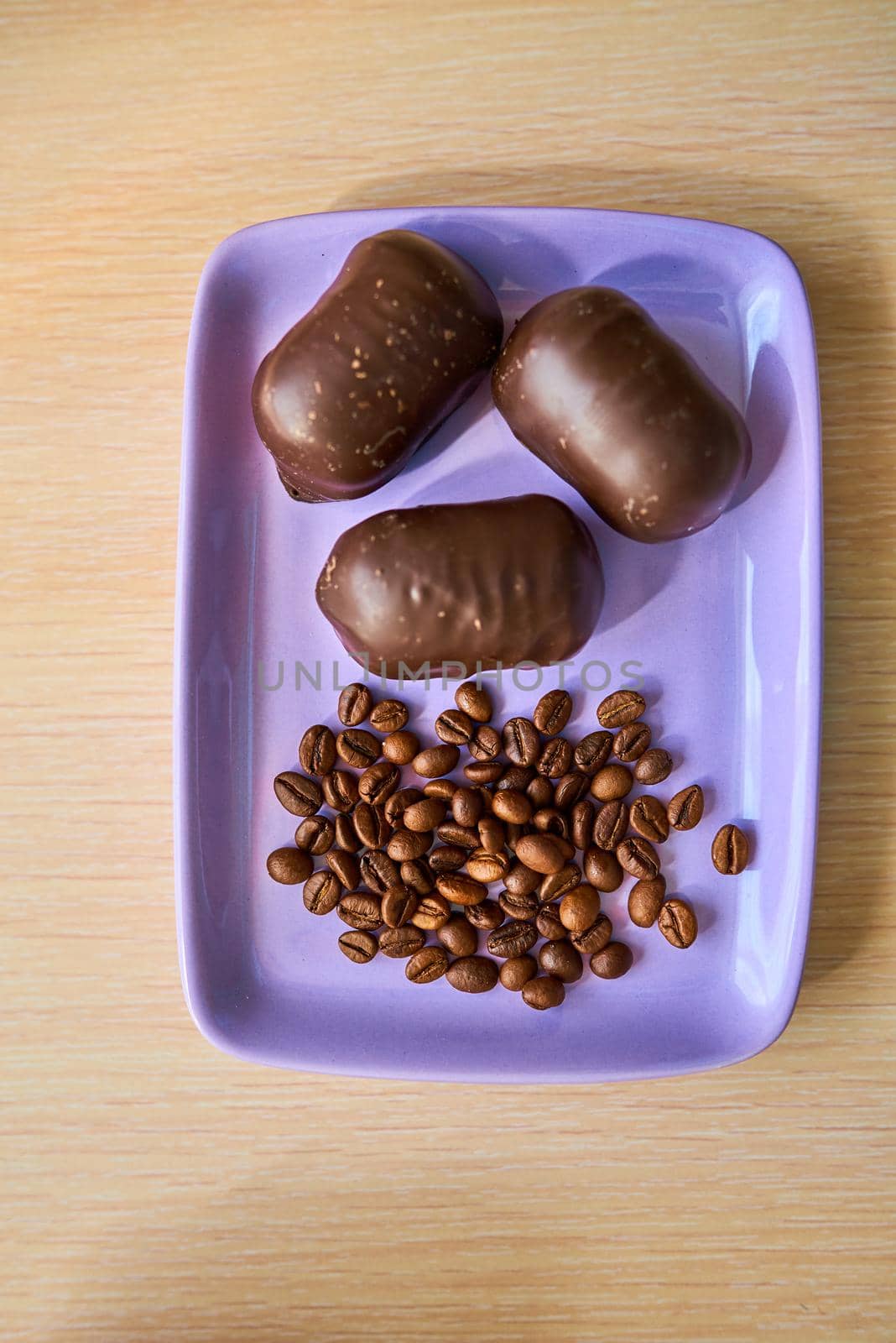 Three chocolates and a handful of coffee beans lie on a purple plate. Top view. Close-up