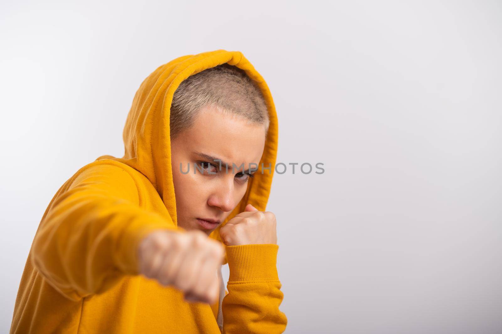 Young woman in ocher hood holding fists near face on white background. Boxer girl is ready for a fight