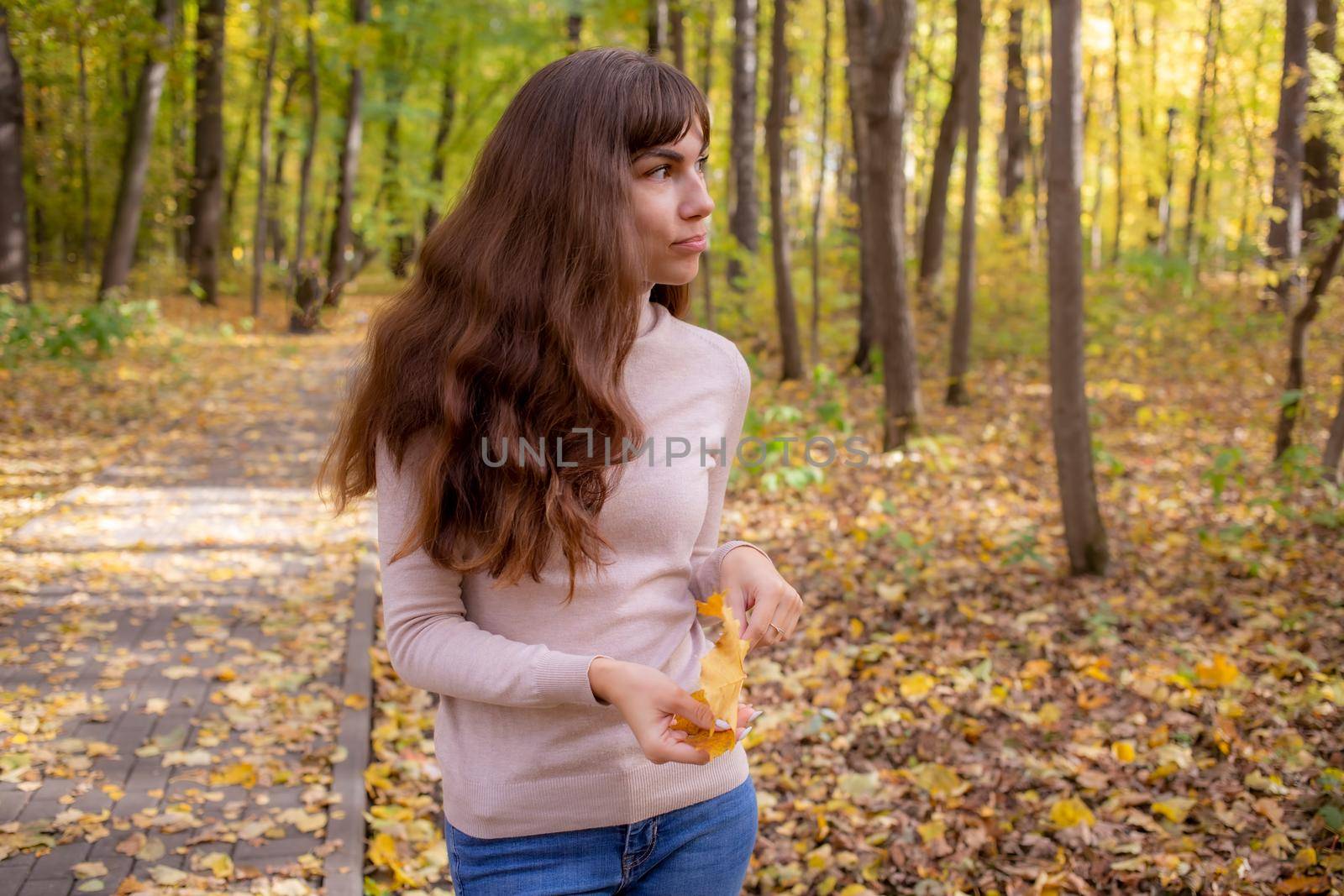 young beautiful woman with autumn leaf smiling in autumn park in sun shines