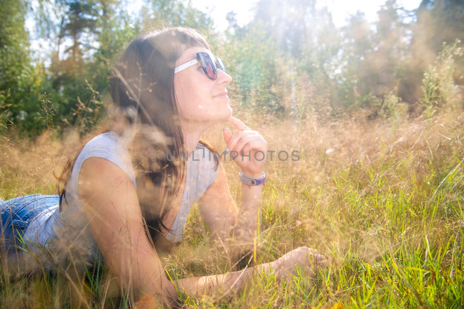 beautiful young woman in sunglasses enjoys the sun on the grass in warm sunshine