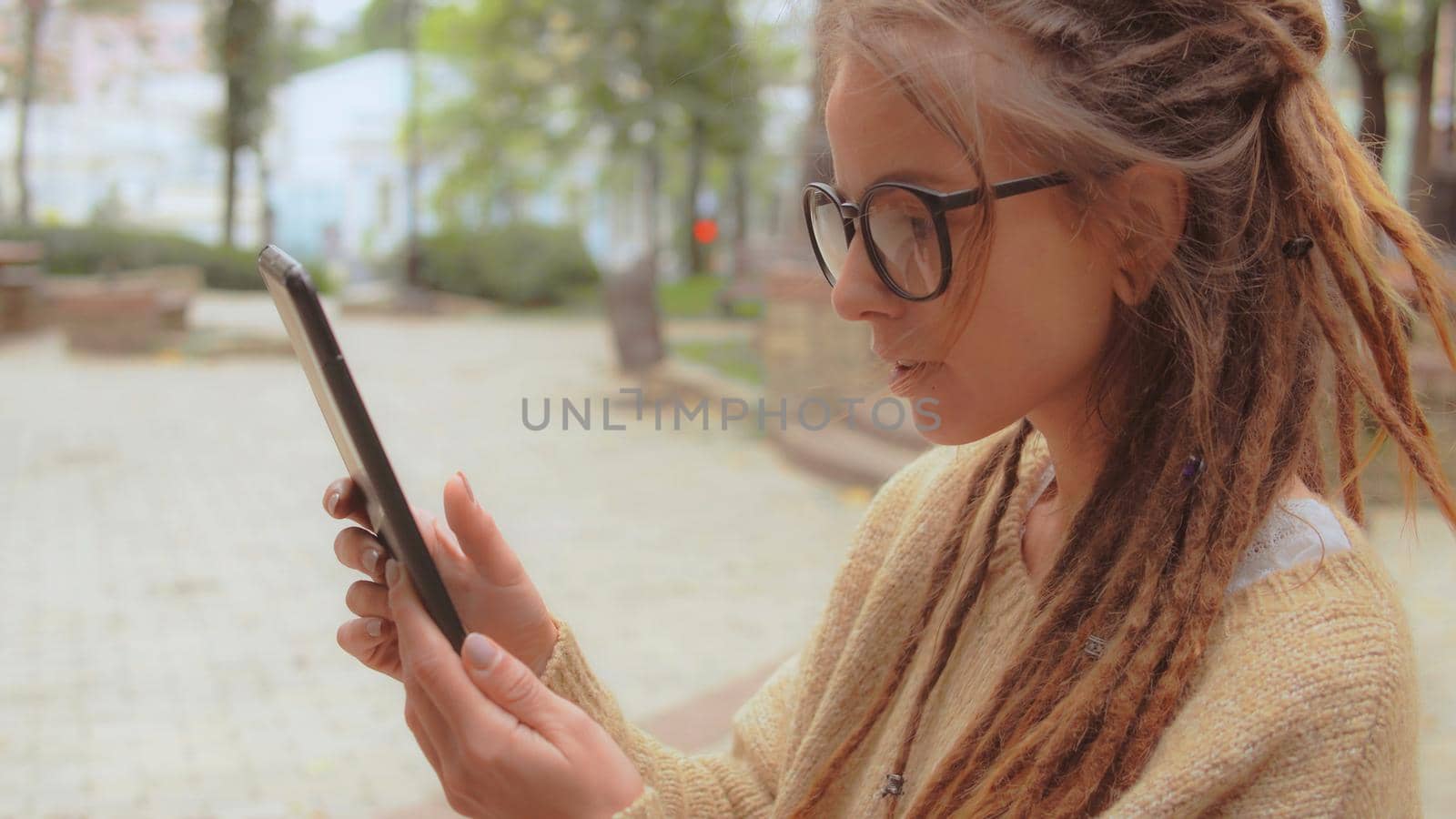 side view smiling young caucasian woman with dreadlocks and eyeglasses using app on digital tablet swipe left and right