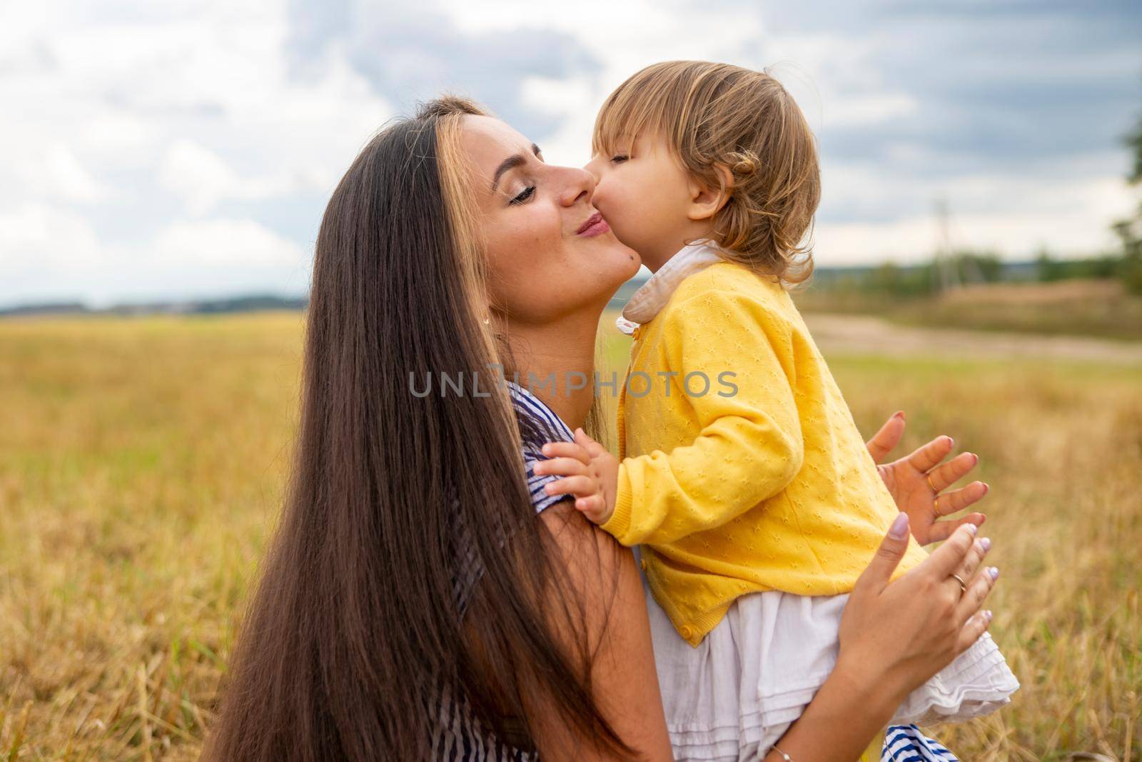 adorable toddler girl kisses her mother on a picnic in the field. by Mariaprovector