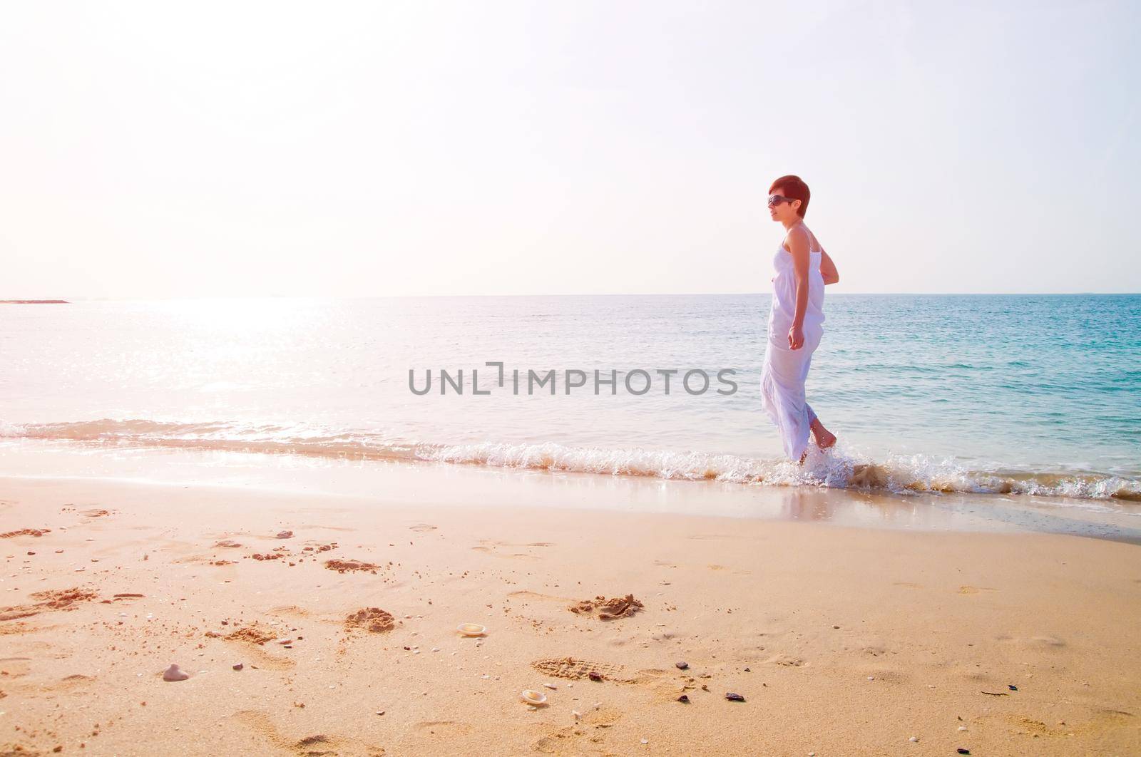 Young brunette woman in summer white dress standing on beach and relaxing at sunset