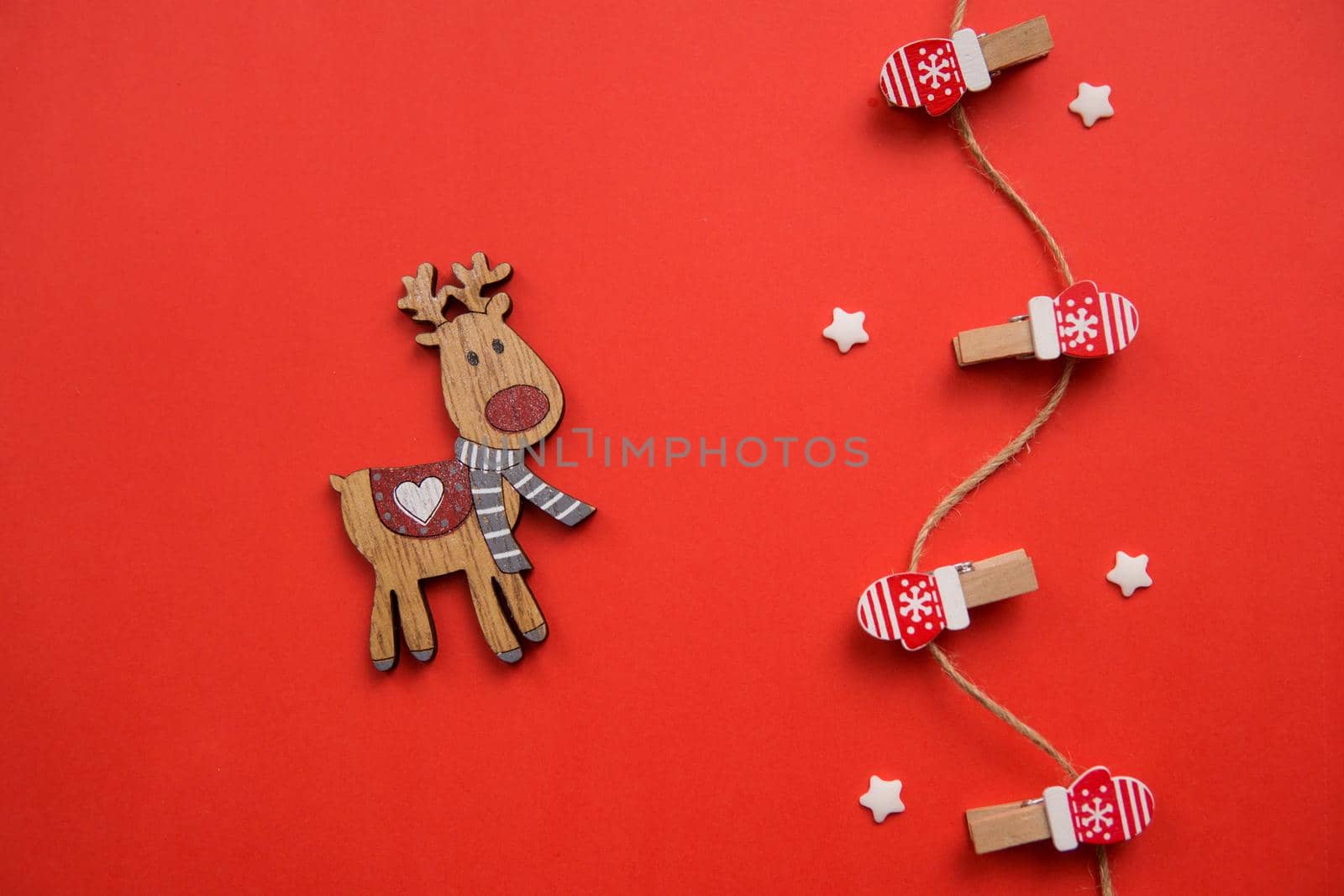 Christmas decorations decorative background. Decorative pins in the form of red gloves and a wooden deer on a red background. Top view, minimalism, flat layout.