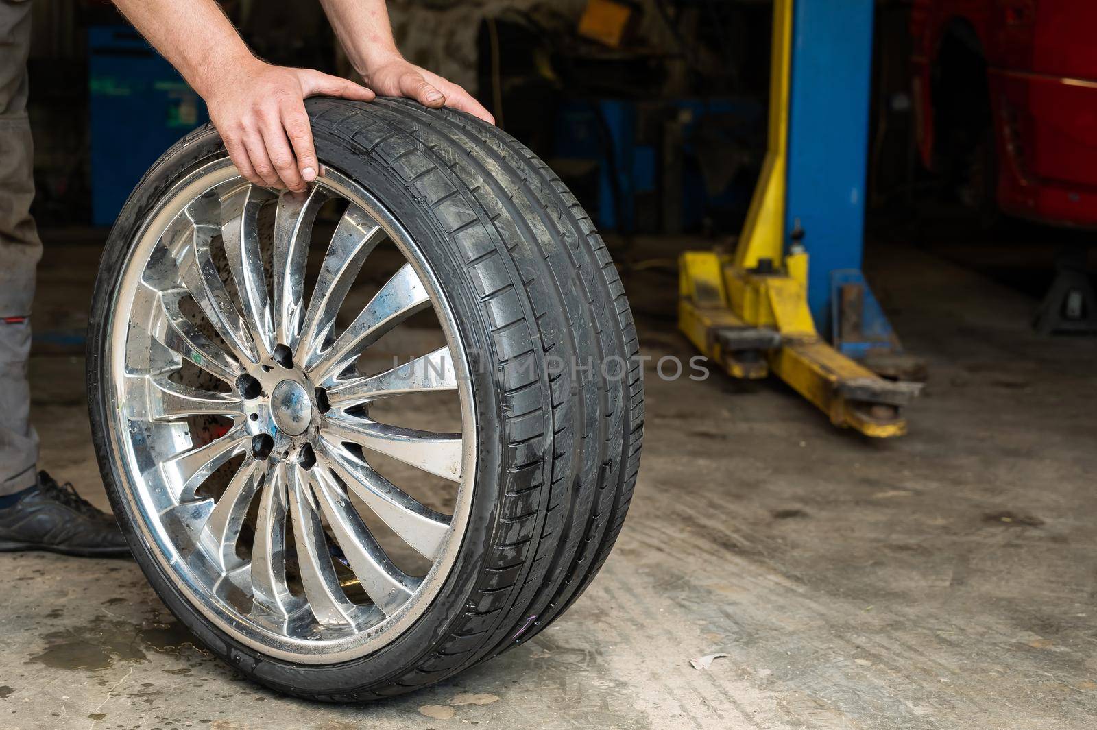 An auto mechanic holds a wheel of a car. Change of car tires according to the season.