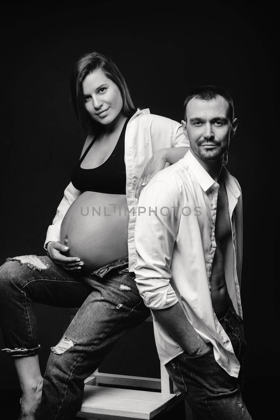 a pregnant woman and a man in a white shirt and jeans in a studio on a black background.