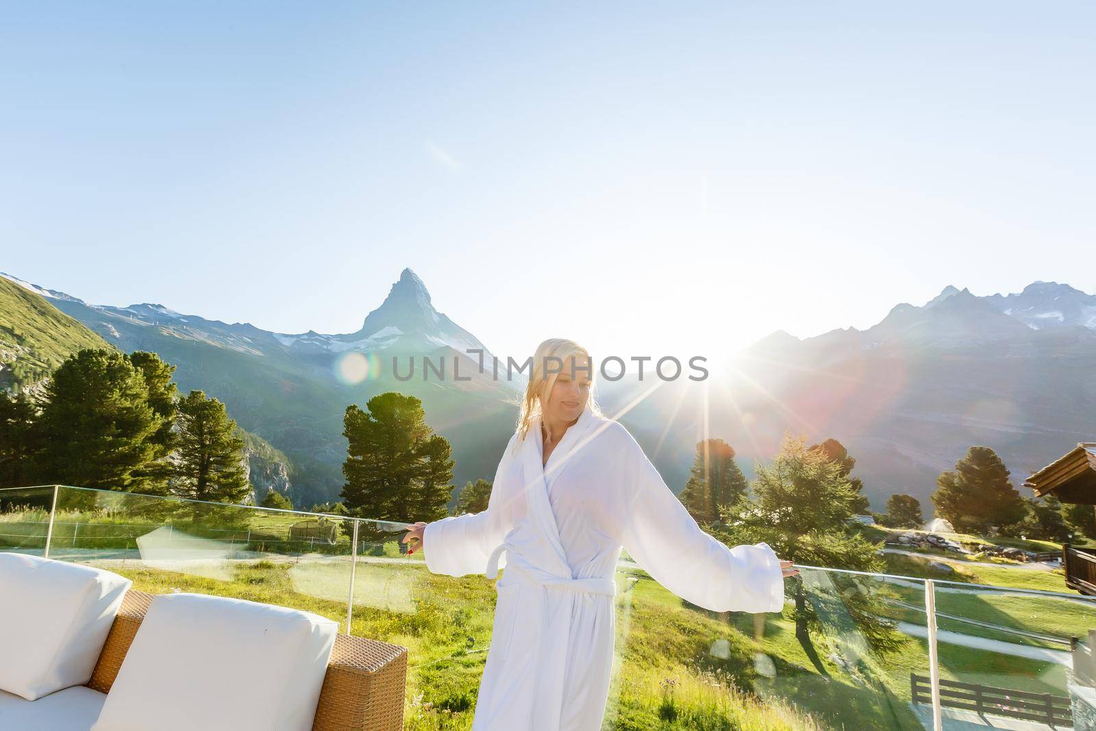 A woman in a white towel is standing on a terrace overlooking the mountains in a hotel room.