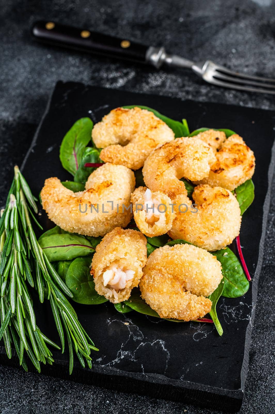Roasted Crispy Shrimps Prawns on a marble board with green salad. Black background. Top view.