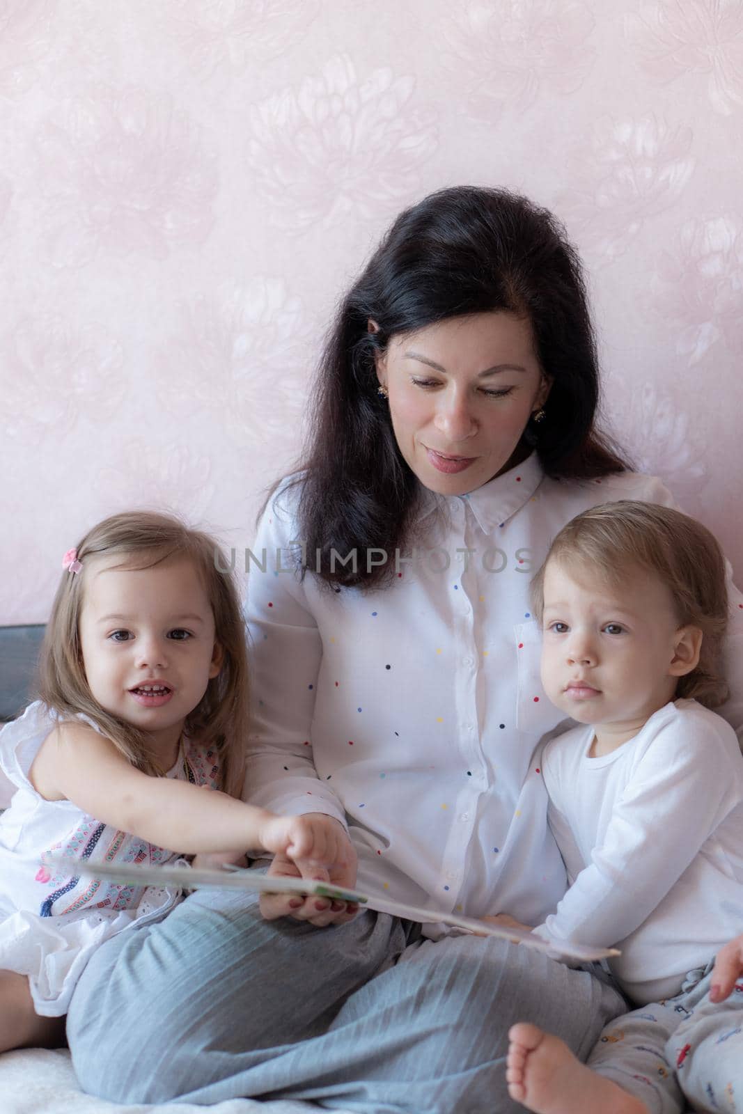 Grandmother with grandson and granddaughter in bed reading a book. Grandmother with grandchildren in bed during distance learning. Grandma plays with her grandchildren in bed during quarantine