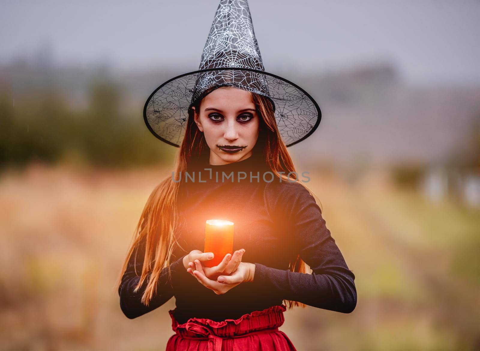 Young girl with halloween makeup holding burning candle on hands on autumn nature