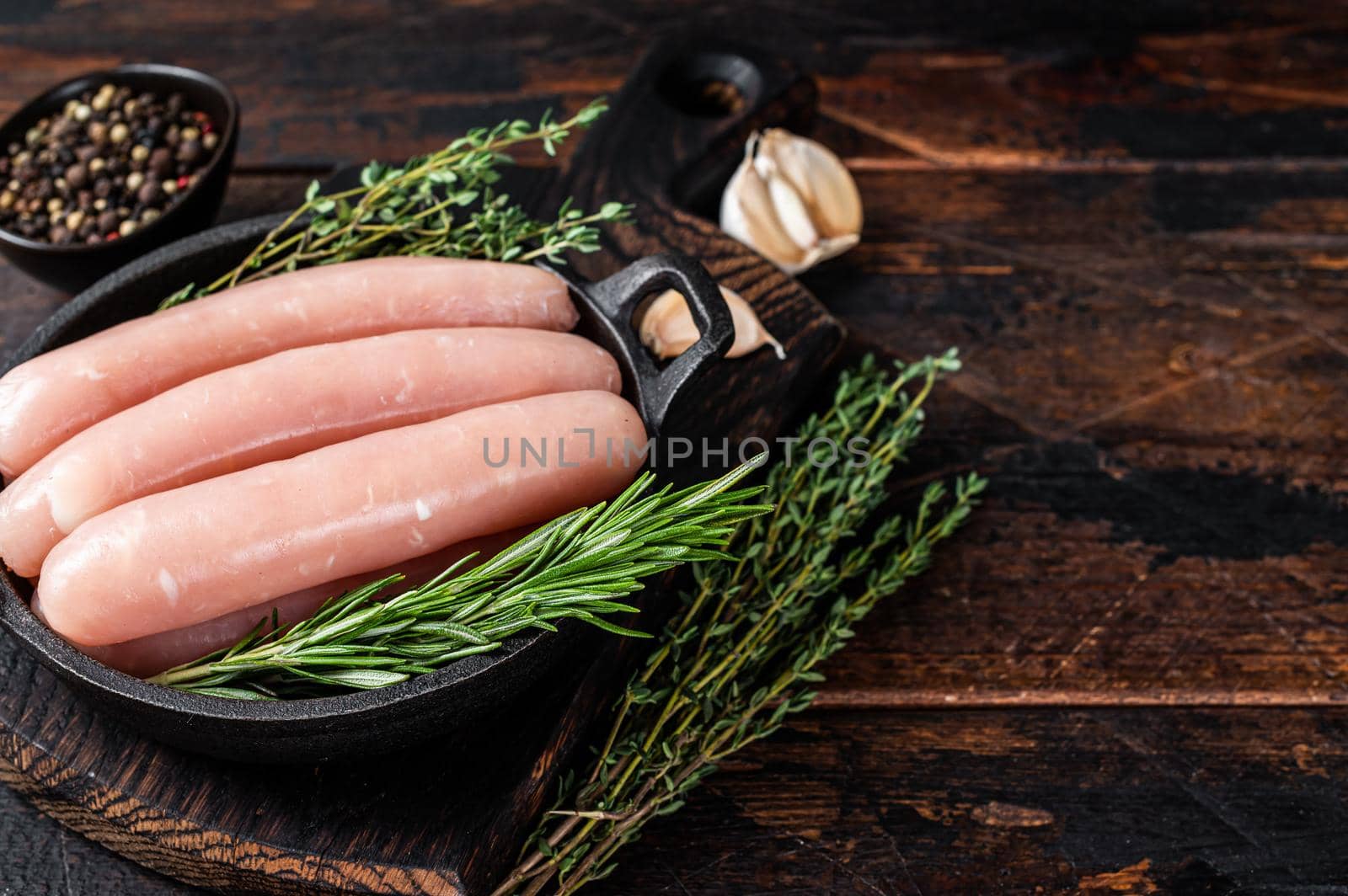 Pork raw sausages in a pan with herbs. Dark wooden background. Top view. Copy space.