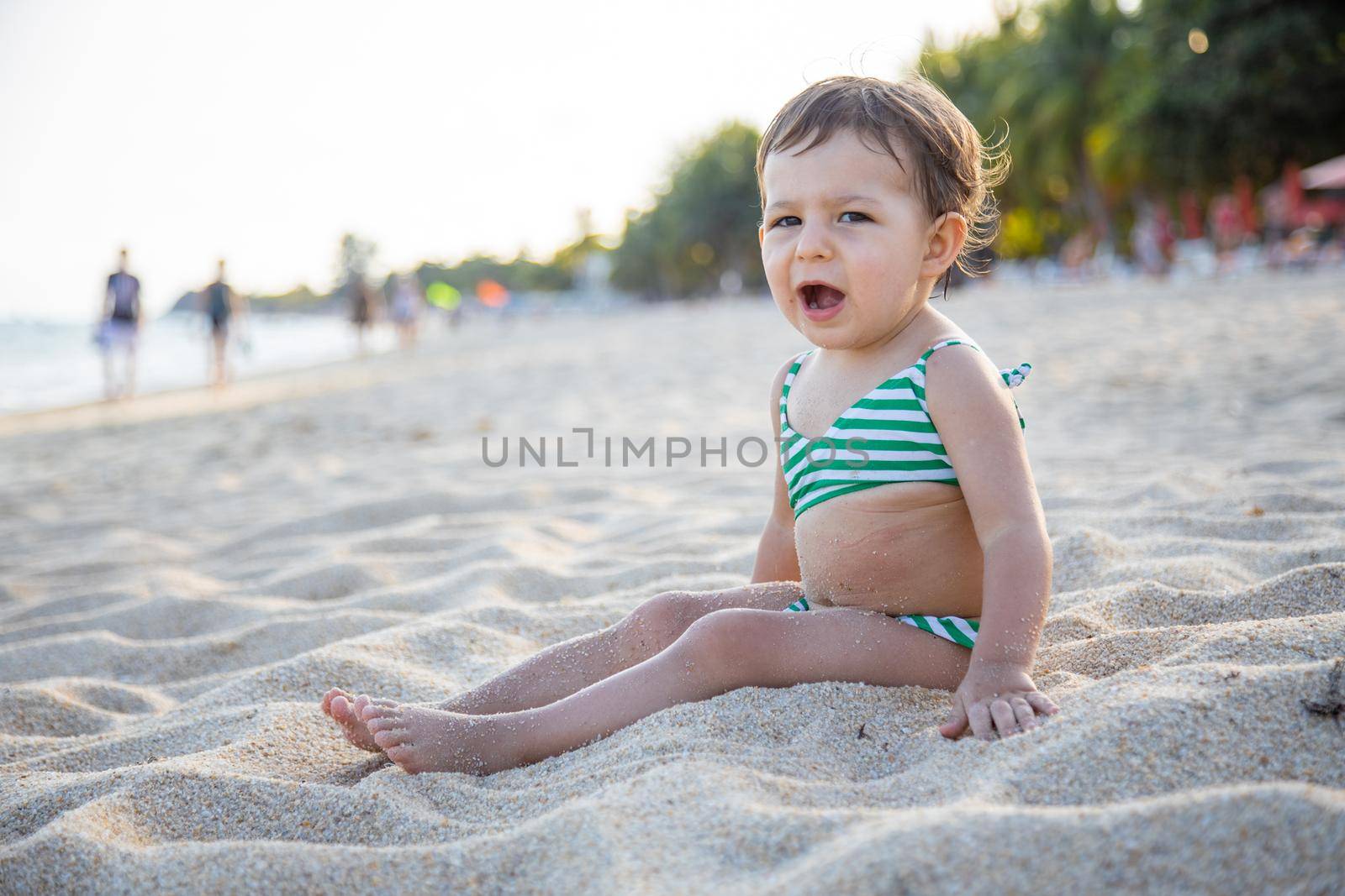 tired toddler girl sitting on sandy bech. little girl yawns on the beach