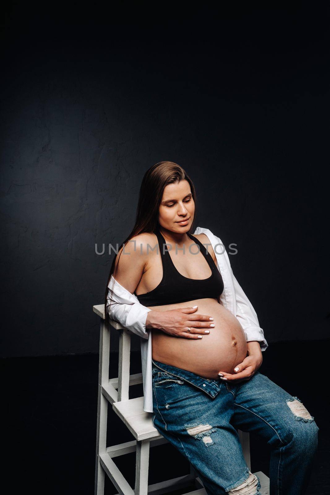 pregnant woman sitting on a ladder chair in a studio on a black background.