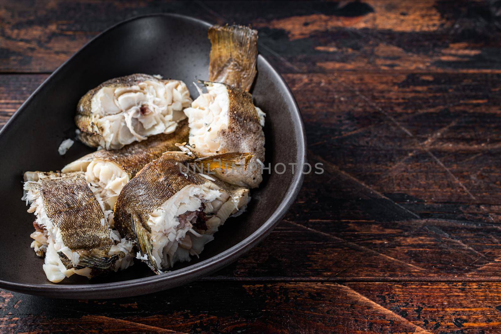 Roasted hake white fish in a plate. Dark wooden background. Top view. Copy space by Composter
