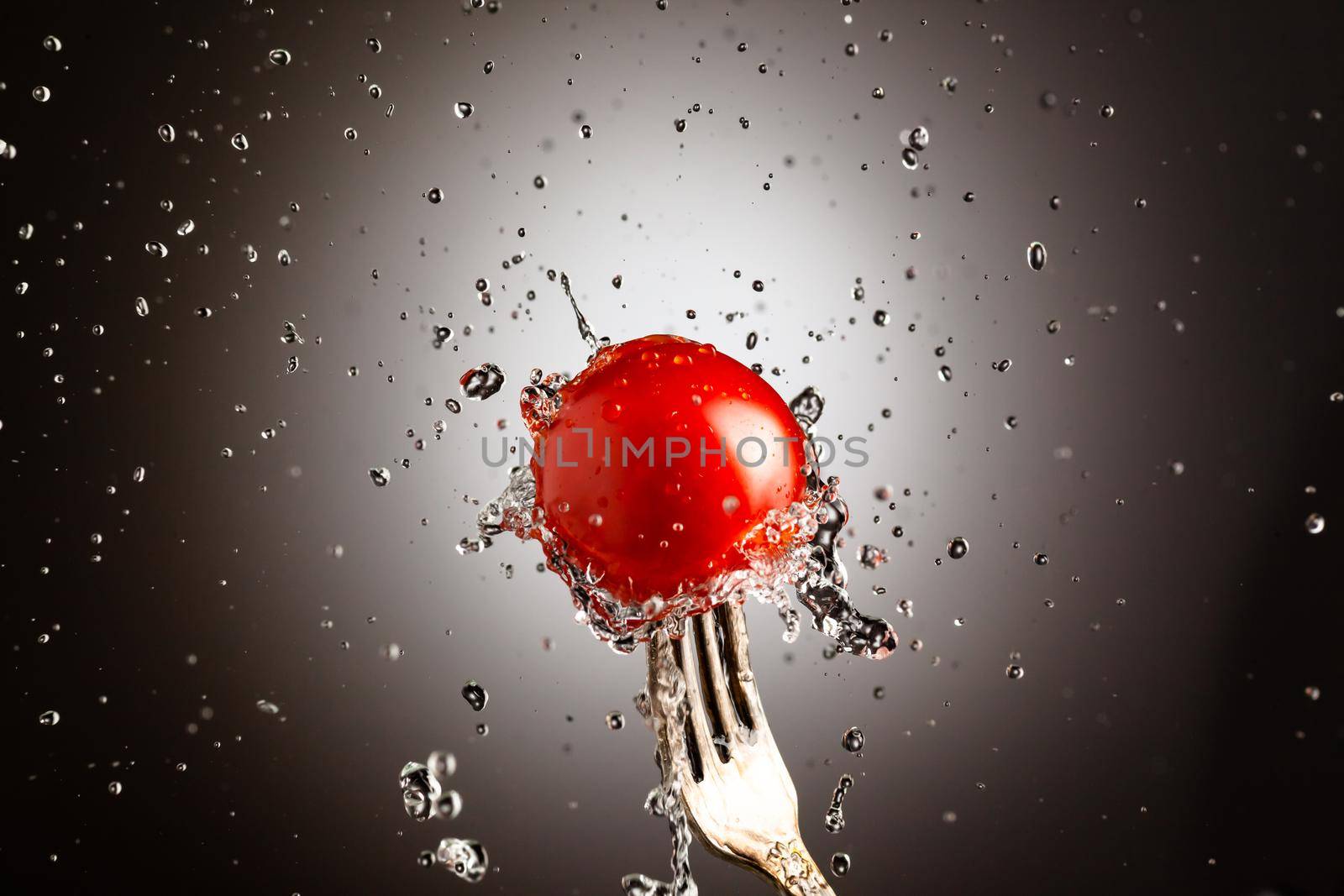 Cherry tomatoes on a metal fork. Splashes of water. Black white background.