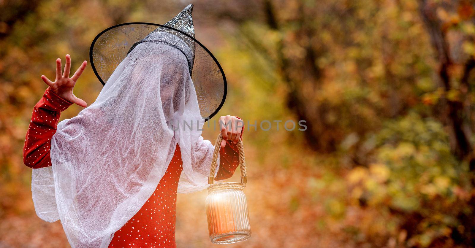 Little girl in halloween costume with candle frighting on autumn nature background