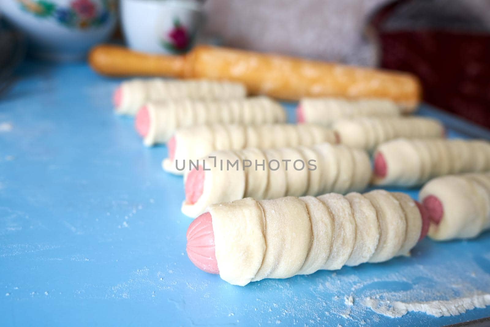 Blanks for fried pies. The sausages are wrapped in thin strips of yeast dough. The dough is rising. Selective focus