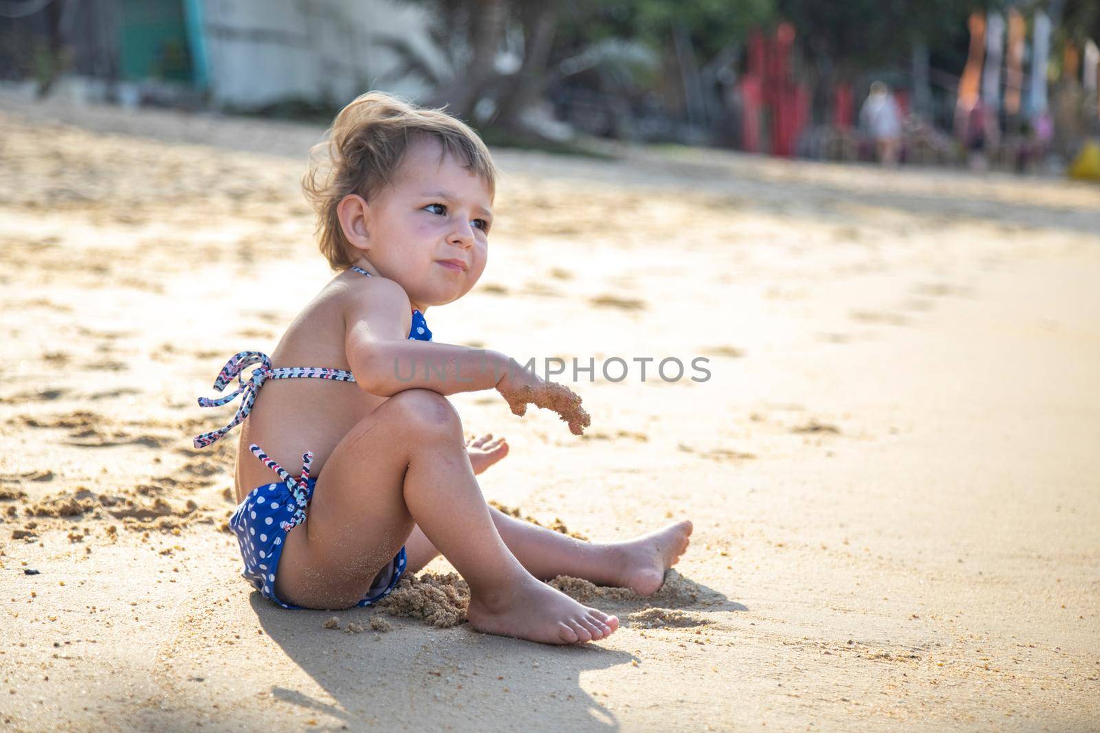 portrait of little cute girl sitting and playing on a beach near the sea on vacations in sunset.