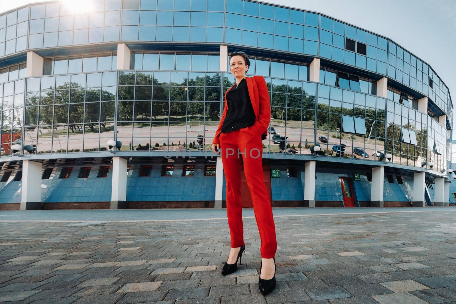 A girl in a red suit stands against the background of a modern building in the city.