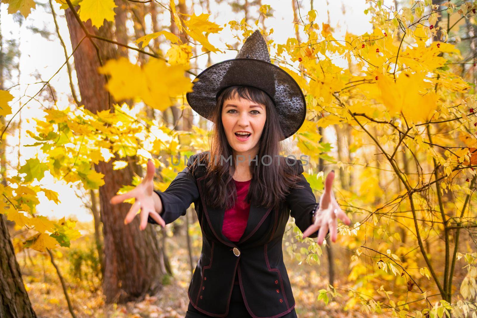 the witch making magic. woman in a witch costume laughs and throws leaves to the camera in the autumn forest. halloween celebration