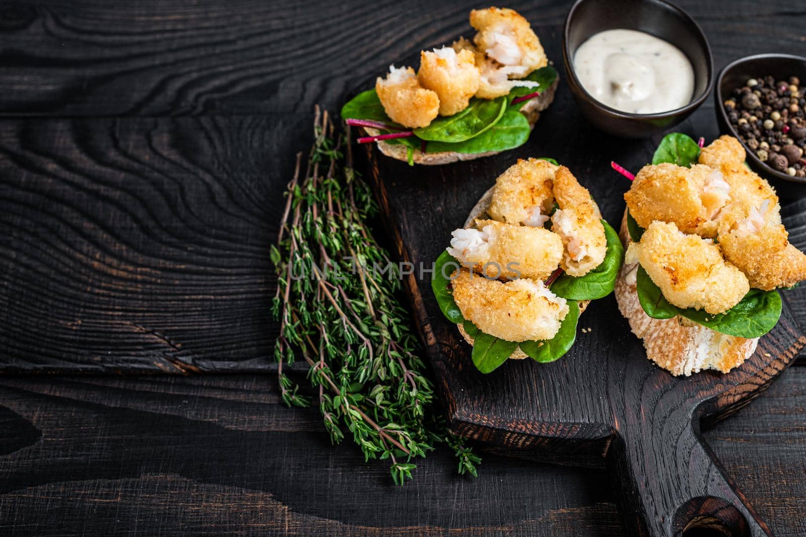 Toasts with Crispy Fried Shrimps Prawns and green salad on a wooden board. Black wooden background. Top view. Copy space.