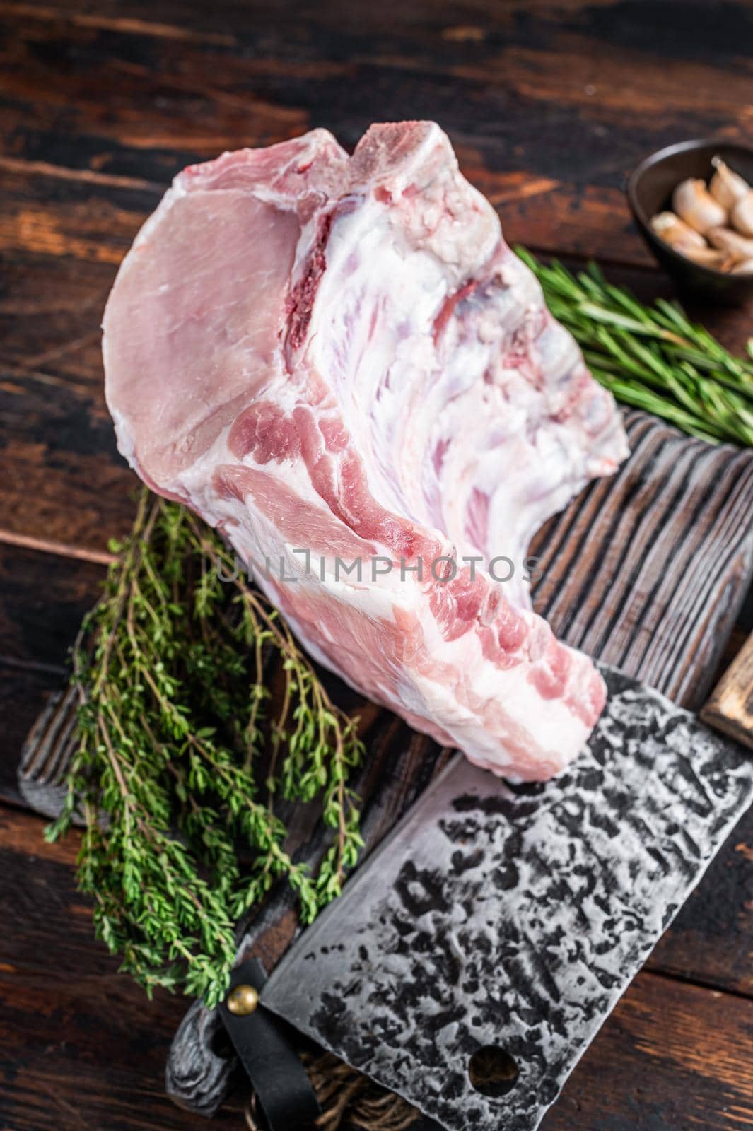 Raw rack of pork loin chops with ribs on a butcher board with meat cleaver. Dark wooden background. Top view by Composter