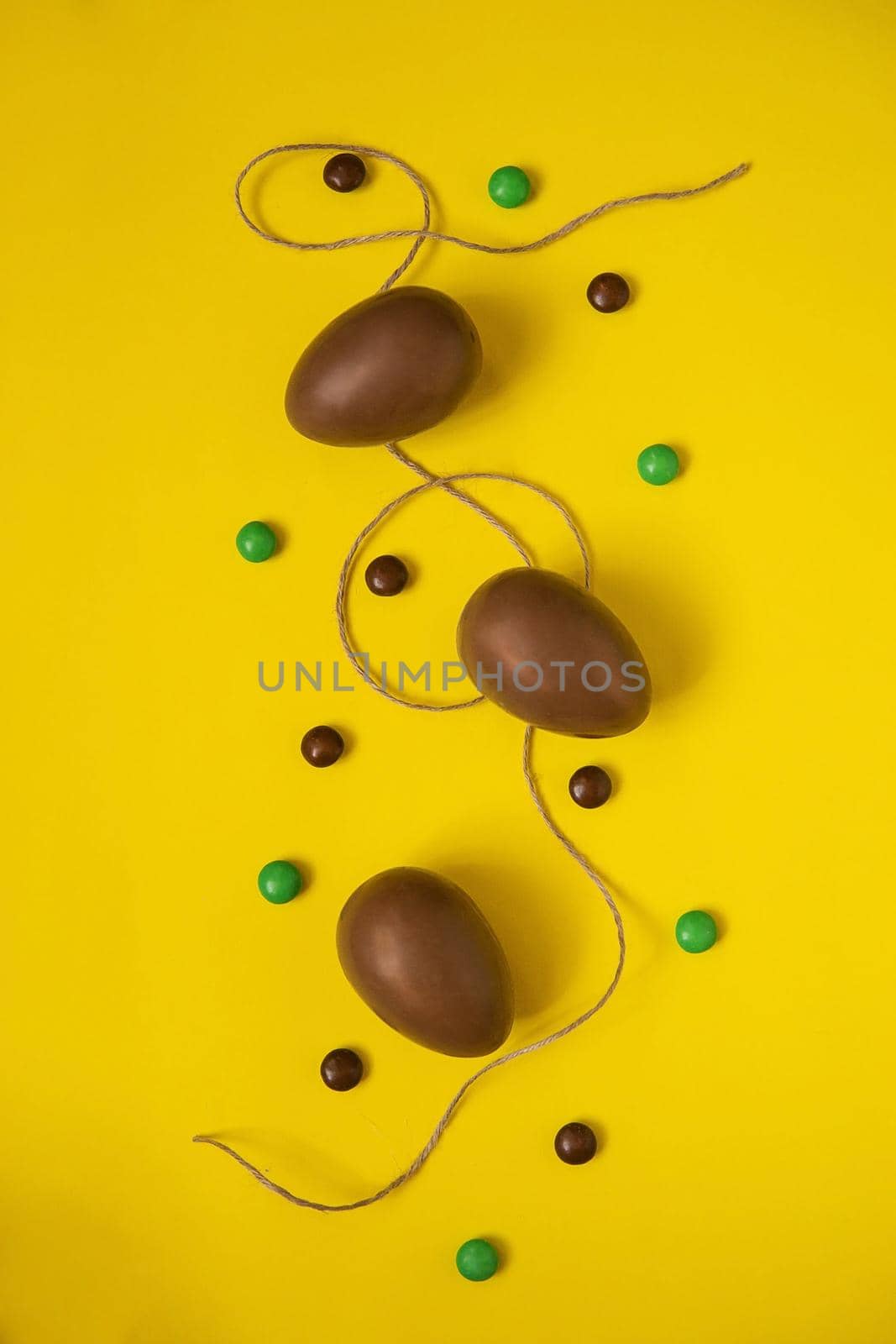 Flat lay composition with chocolate Easter eggs and chocolate sweets on yellow background. View from above, empty space for text. by Annu1tochka