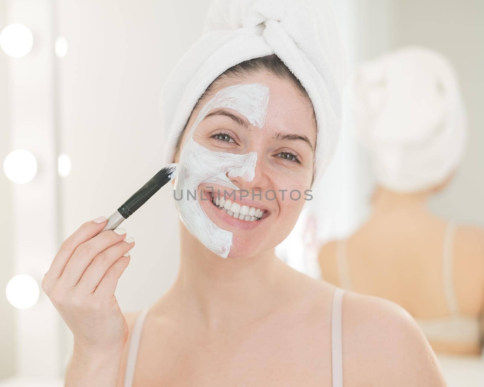 Beautiful caucasian woman with a towel on her hair applies a clay face mask. Taking care of beauty at home by mrwed54