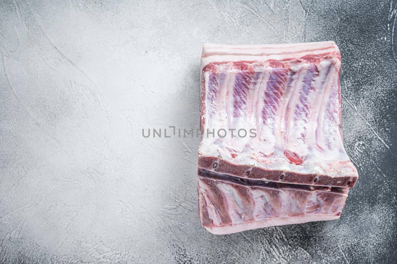 Raw whole rack of pork loin with ribs on kitchen table. White background. Top view. Copy space by Composter