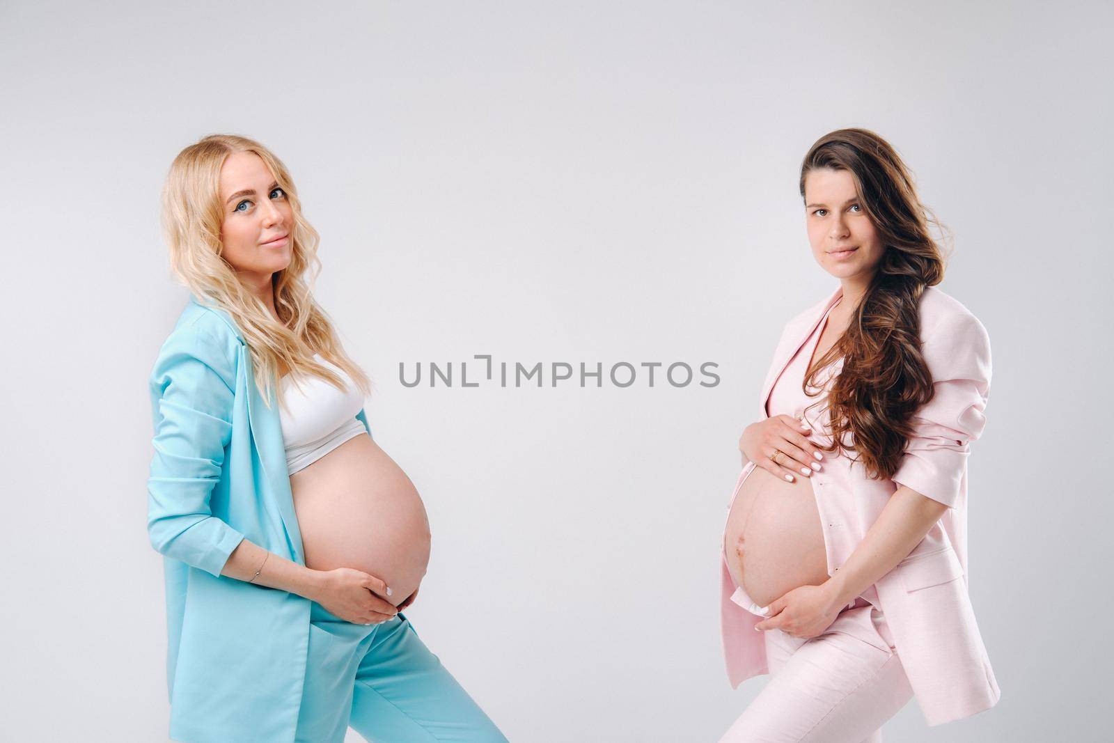 Two pregnant women with big bellies in suits on a gray background.