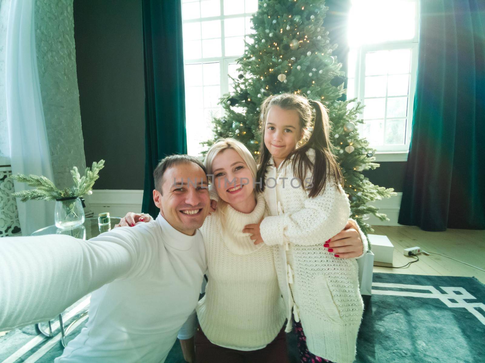 family, holidays, technology and people - smiling mother, father and little girl making selfie with camera over living room and christmas tree background by Andelov13