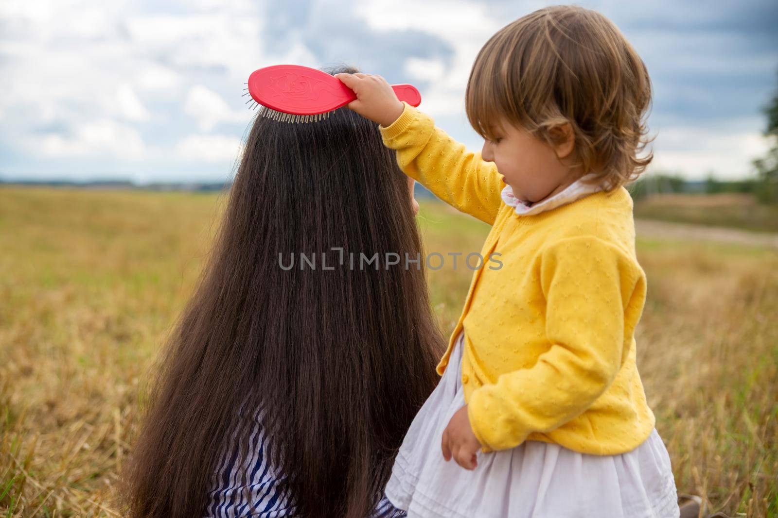 adorable toddler girl combing her mom's hair outdoors outdoors on a sunny day. mother and daughter love concept