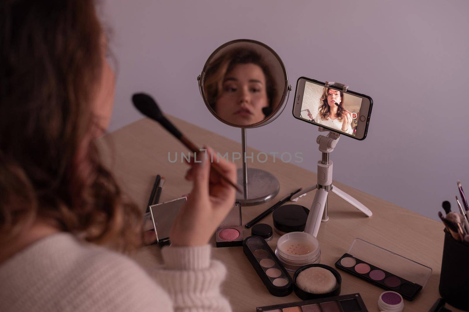 Caucasian woman leads an online make-up lesson for herself on her mobile phone by mrwed54