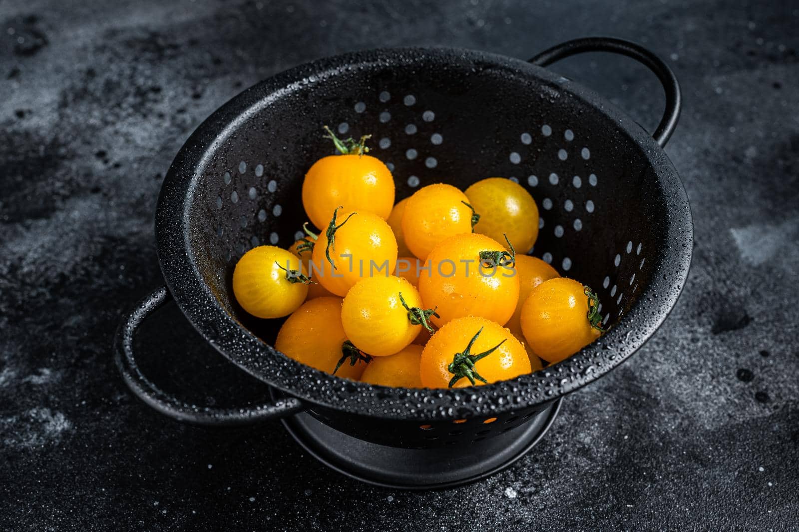 Yellow cherry tomato in a colander. Black background. Top view by Composter