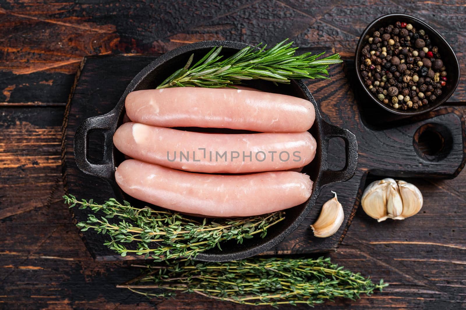 Pork raw sausages in a pan with herbs. Dark wooden background. Top view by Composter