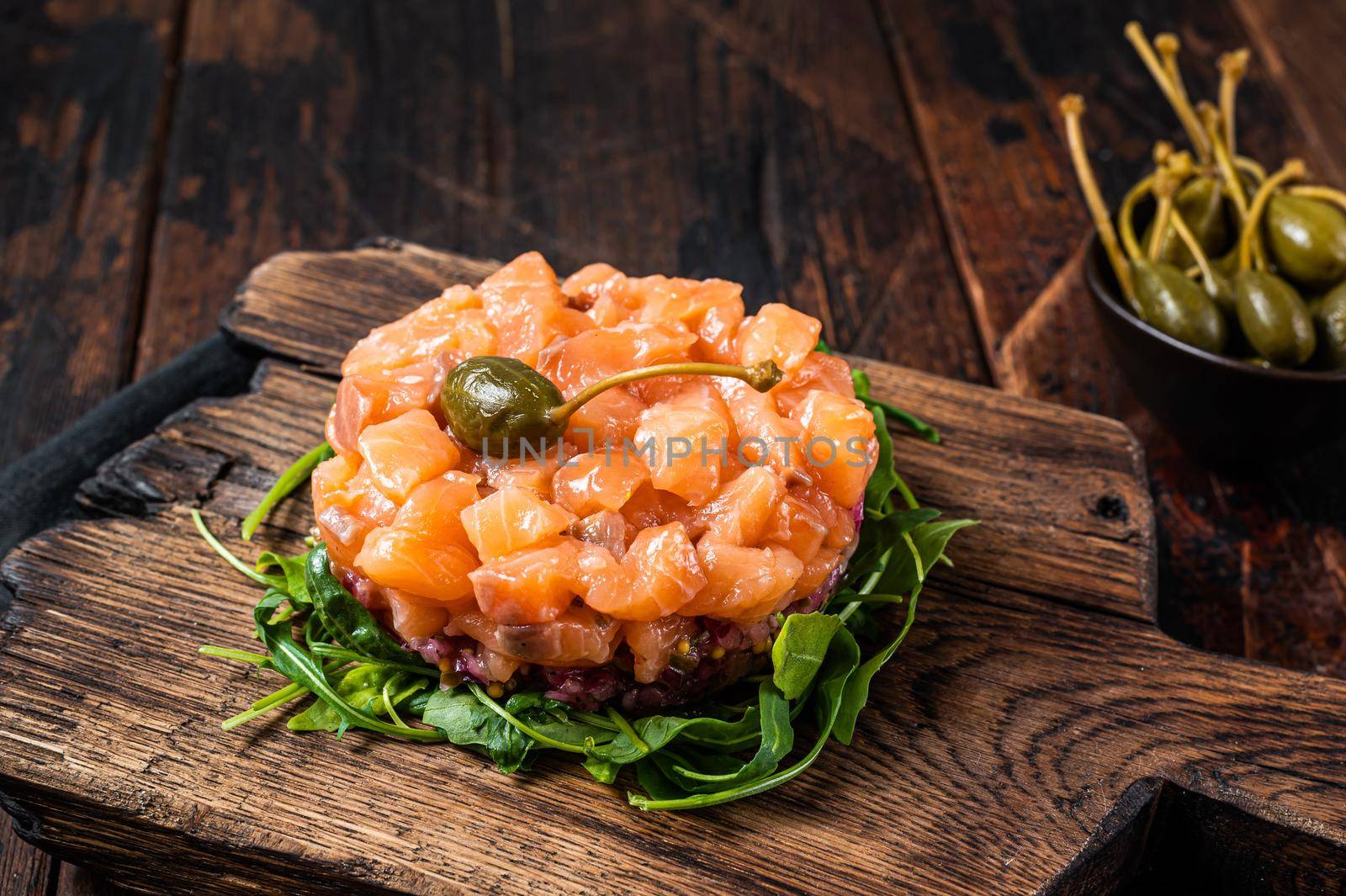 Salmon tartare or tartar with red onion, avocado, arugula and capers. Dark wooden background. Top View by Composter