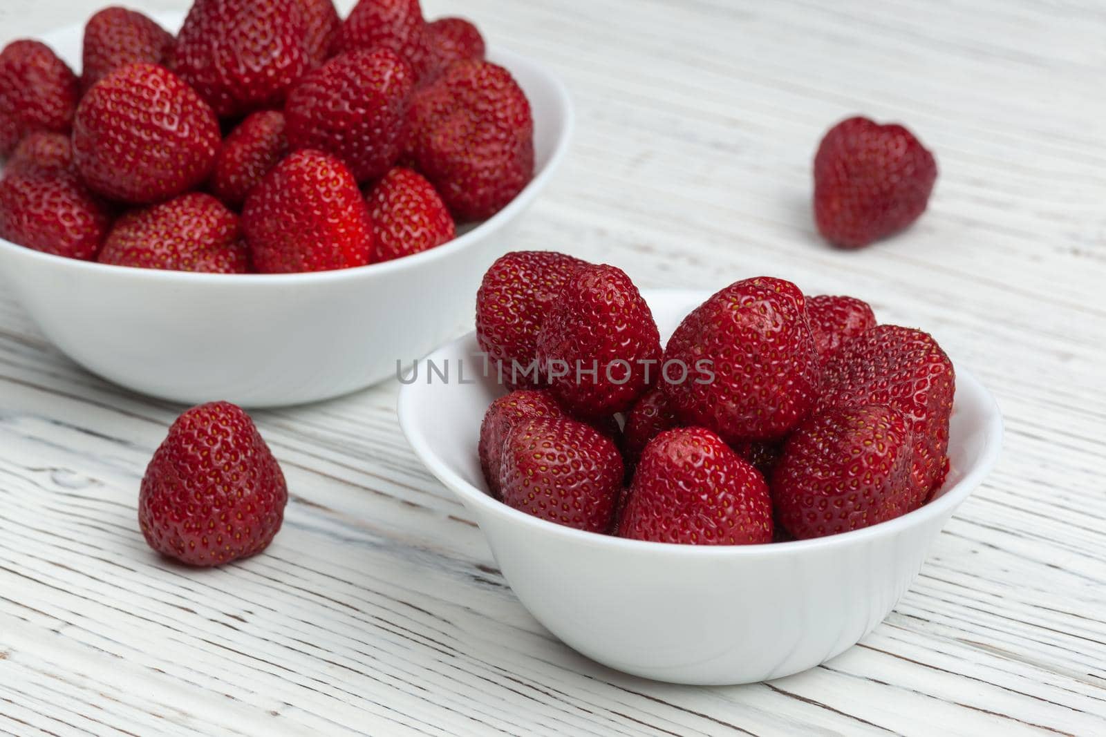 two white plates with strawberries on a wooden background, next to lie two strawberries