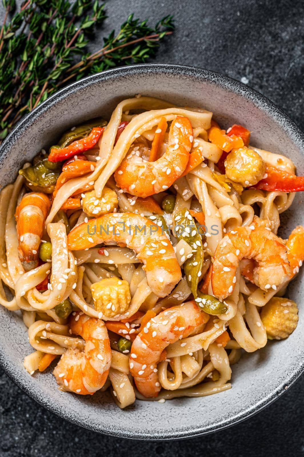 Chinese wok Stir-fry udon seafood noodles with shrimp prawns in a bowl. Black background. Top view by Composter