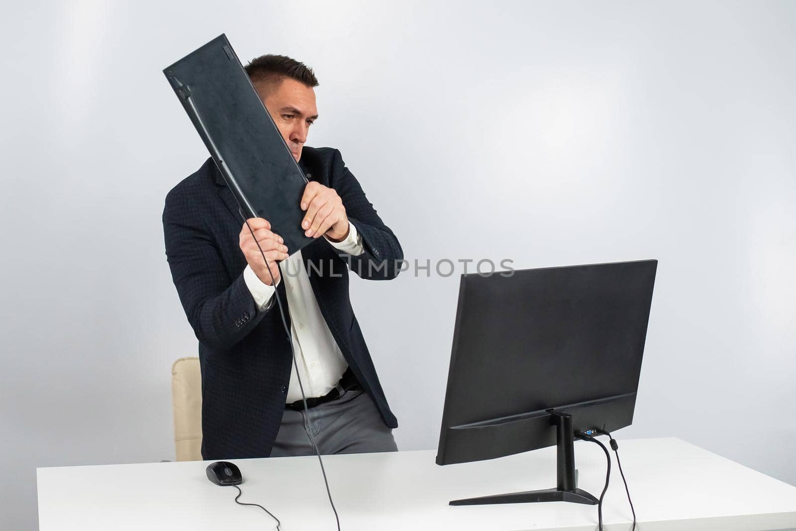 Caucasian man in a suit gets angry and smashes the keyboard on the monitor. An office worker in a rage breaks the computer