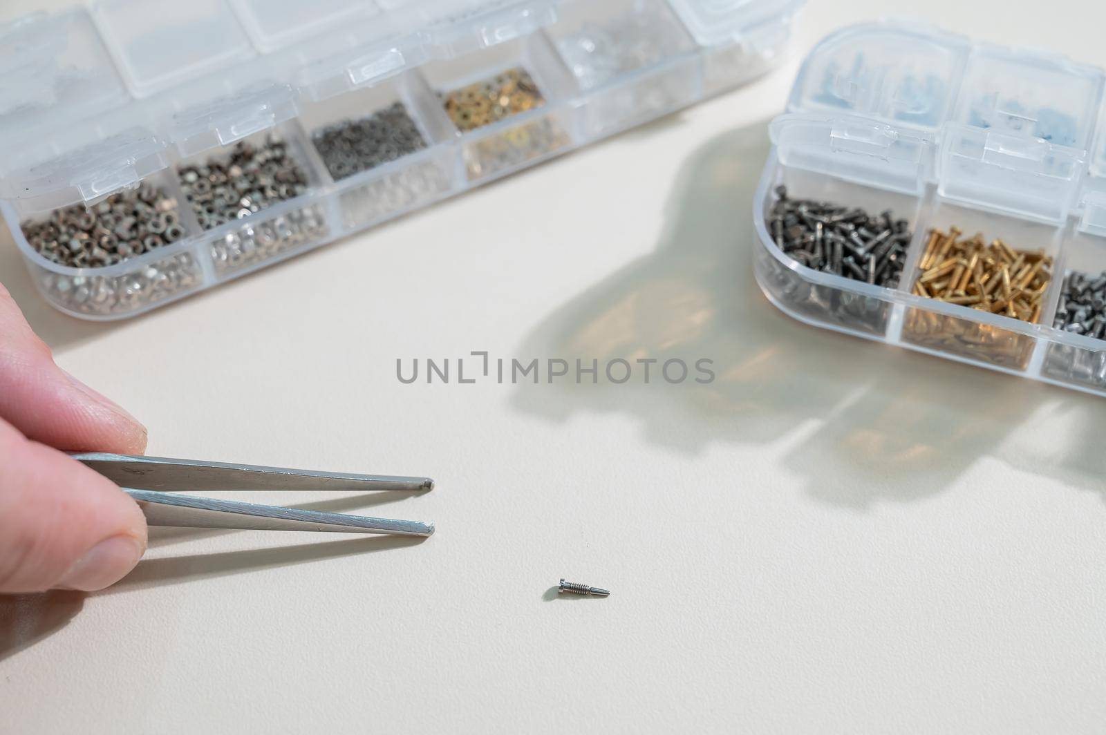 A close-up of male hands takes a screw for repairing glasses with tweezers by mrwed54