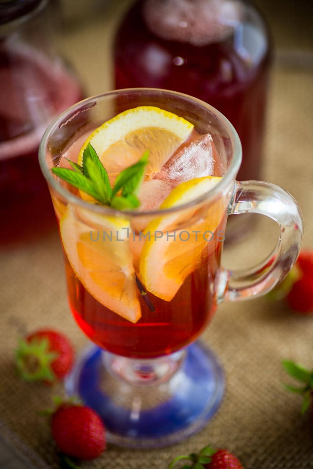 refreshing cool strawberry lemonade with lemon, ice and mint in a glass on a wooden table
