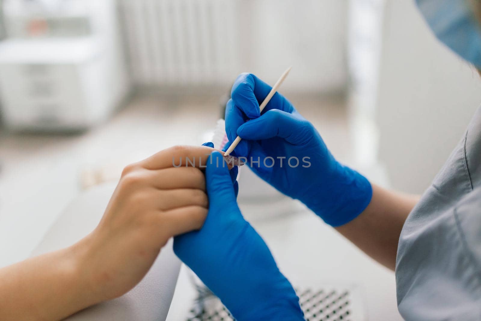 Manicurist wearing protective mask painting female nails with nail polish in manicure salon.
